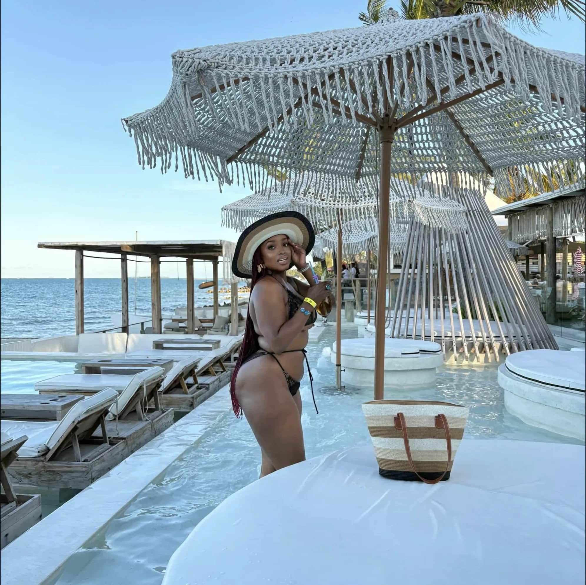 Woman in a black bikini and sun hat at a beachfront pool bar