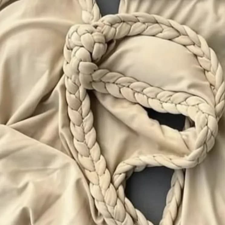 Close crop of a hand-braided cord tie coiled across soft sand-coloured swim fabric